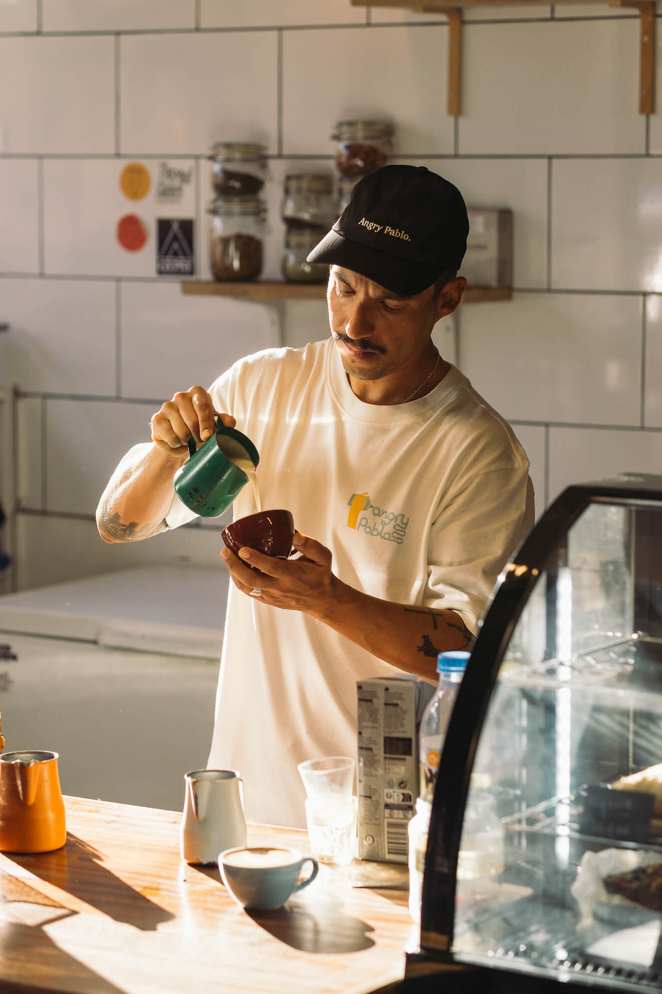 Barista pouring milk wearing an Angry Pablo black cap